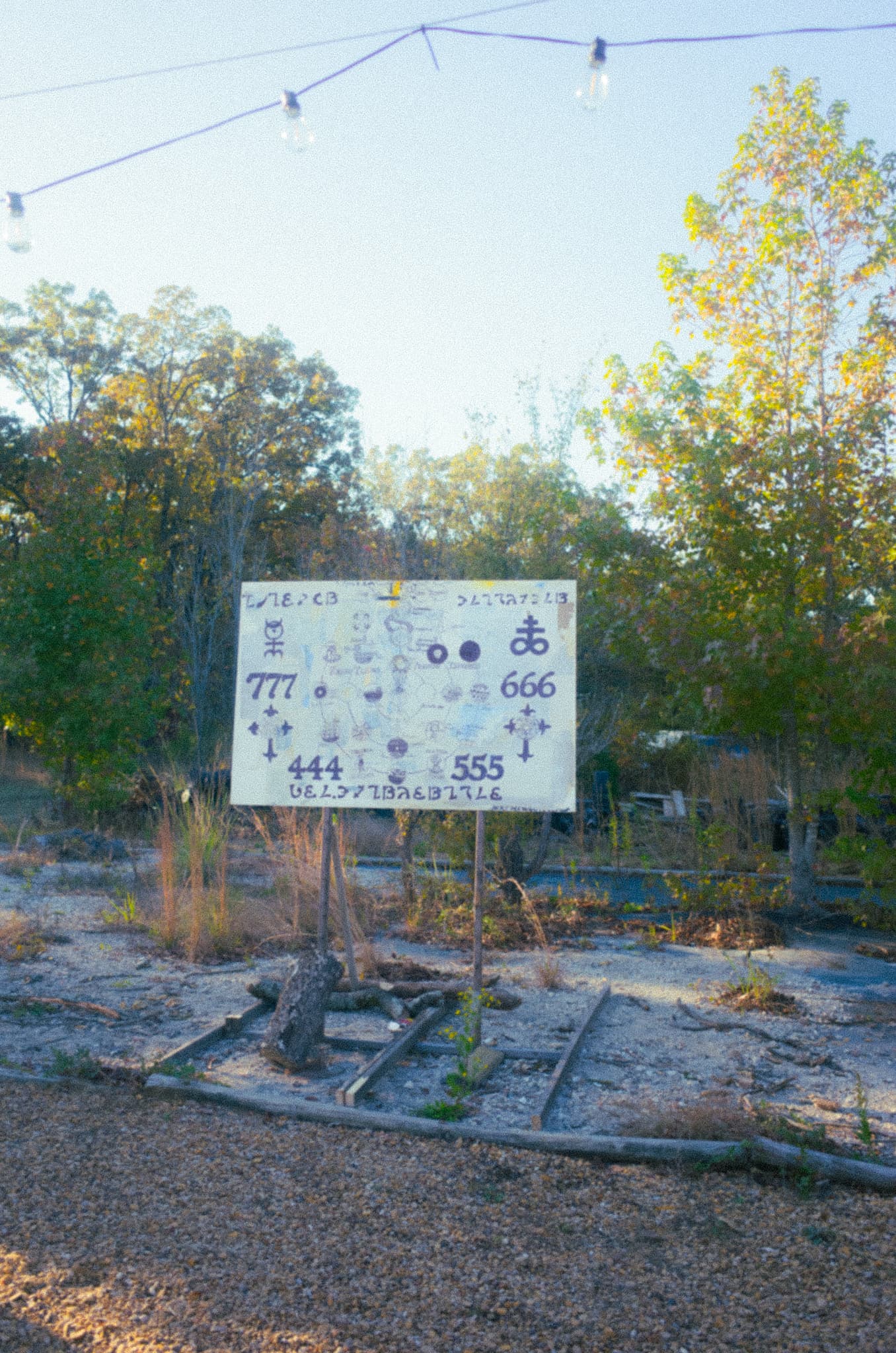 A hand-painted sign covered in occult numerology and symbols in a sunlit field